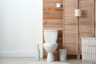 Photo of Toilet bowl near wooden wall in modern bathroom interior. Space for text