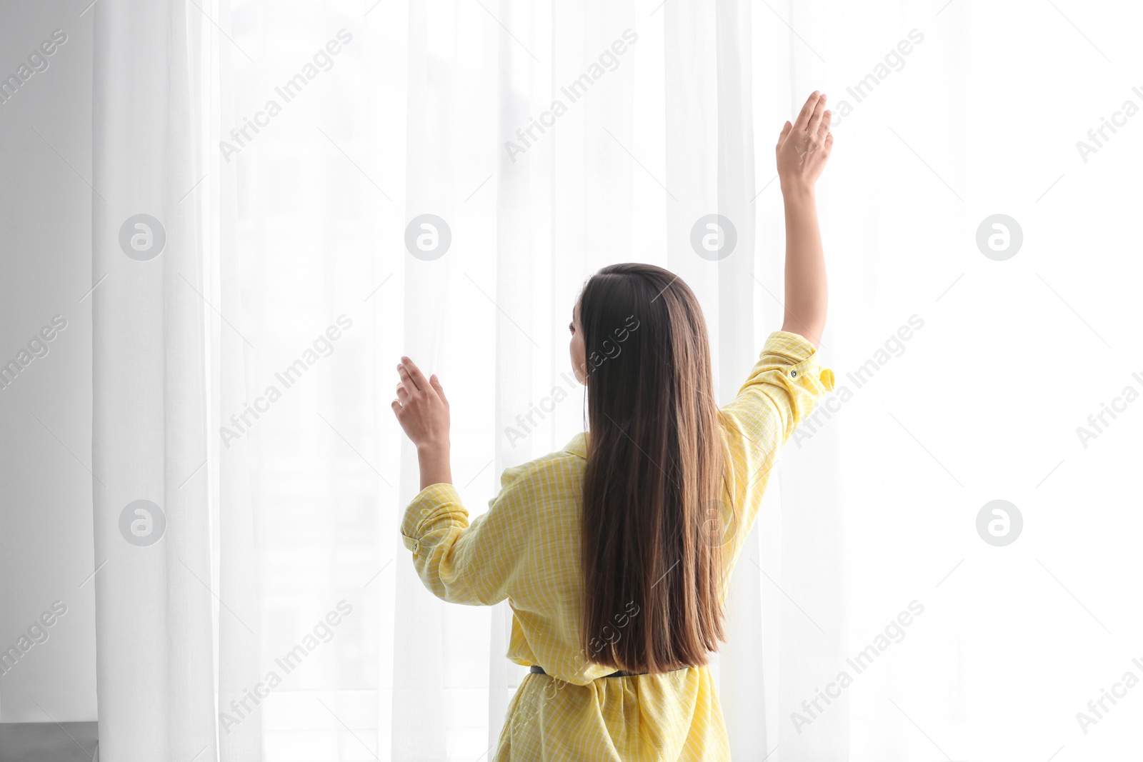 Photo of Young woman near window with curtains indoors