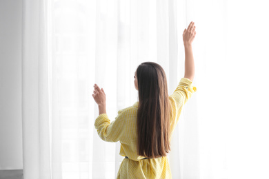Photo of Young woman near window with curtains indoors
