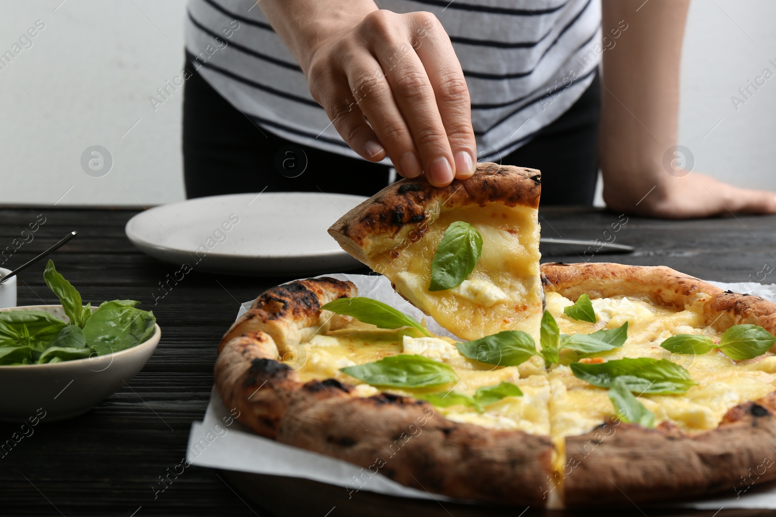 Photo of Woman taking slice of delicious cheese pizza at black wooden table, closeup