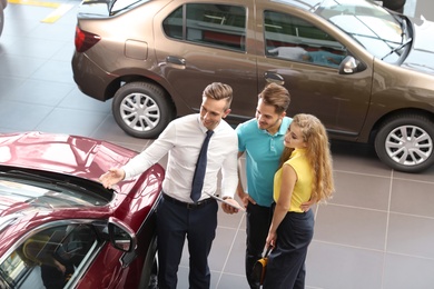 Photo of Young car salesman working with clients in dealership