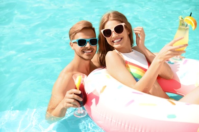 Photo of Young couple with cocktails in pool on sunny day