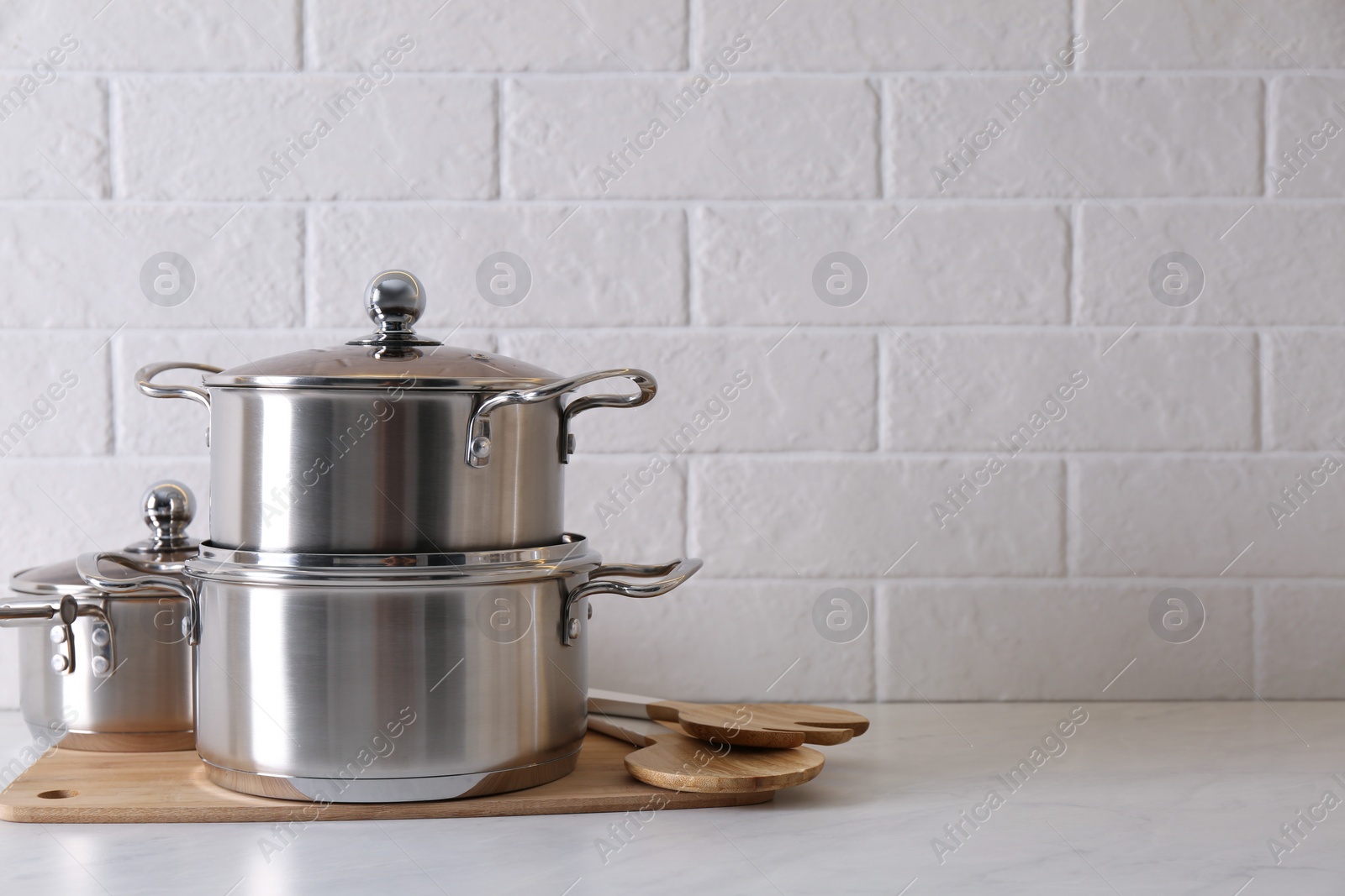 Photo of Set of stainless steel cookware and kitchen utensils on table near white brick wall, space for text