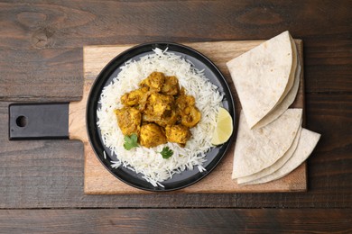 Photo of Delicious chicken curry with rice and tortillas on wooden table, top view