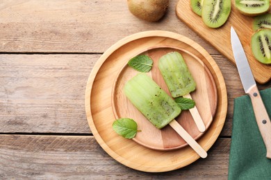 Photo of Flat lay composition with tasty kiwi ice pops on wooden table, space for text. Fruit popsicle
