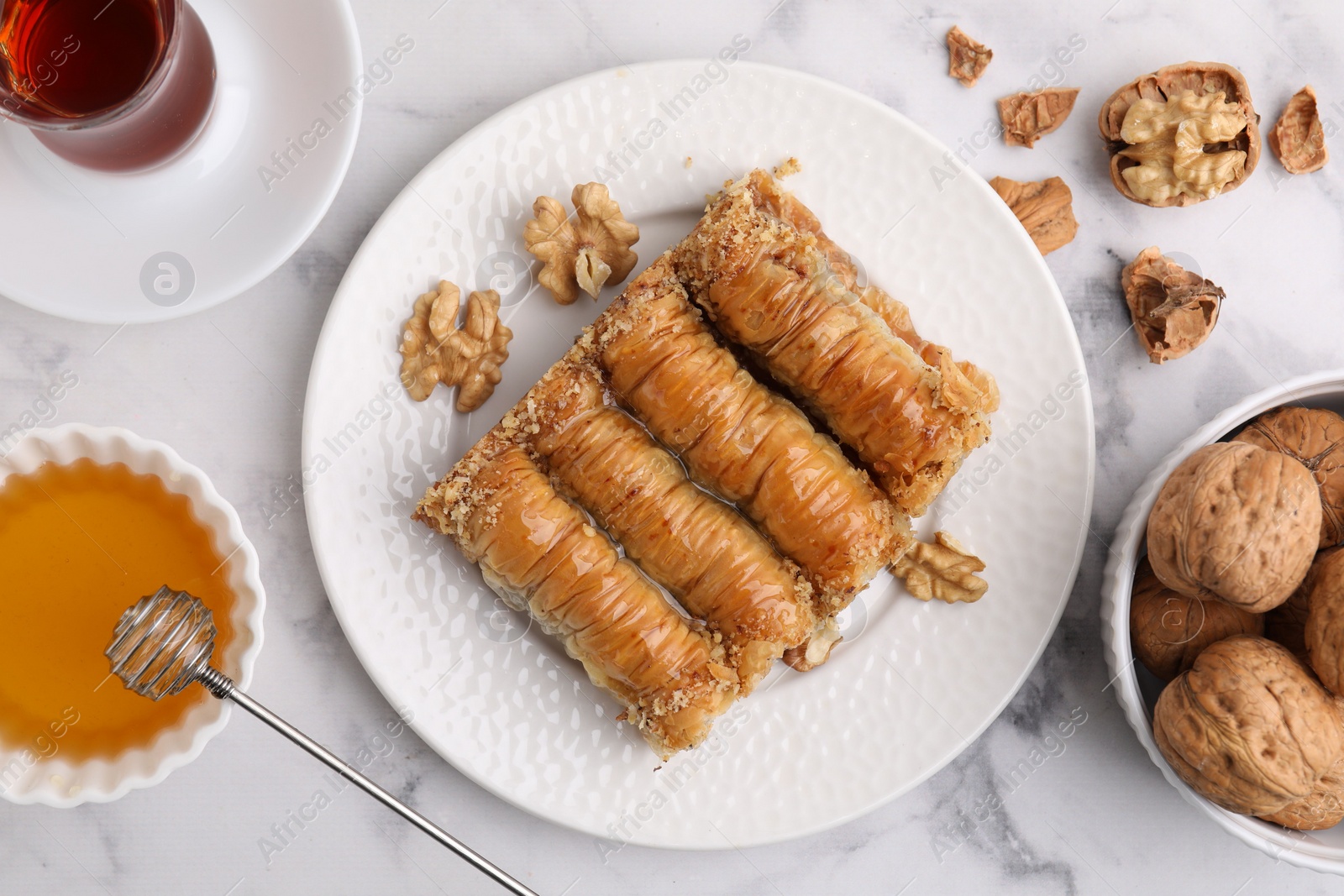 Photo of Eastern sweets. Pieces of tasty baklava, walnuts and tea on white marble table, flat lay