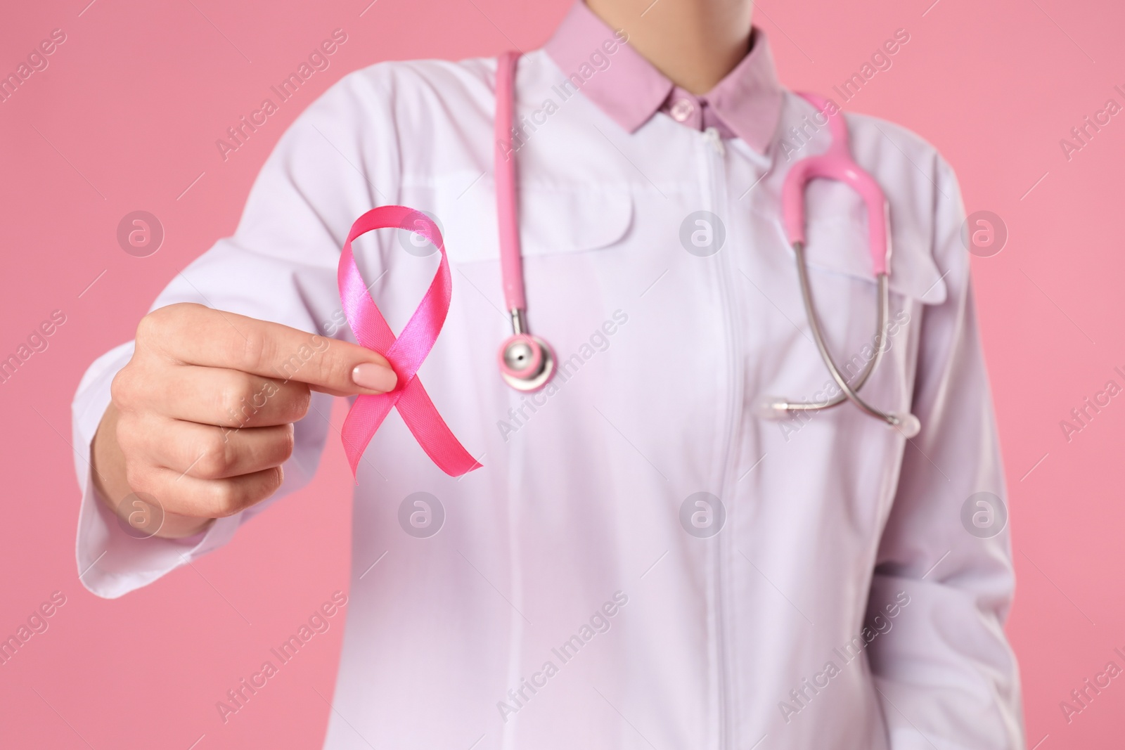 Photo of Doctor with pink ribbon and stethoscope on color background, closeup. Breast cancer awareness