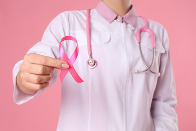 Doctor with pink ribbon and stethoscope on color background, closeup. Breast cancer awareness