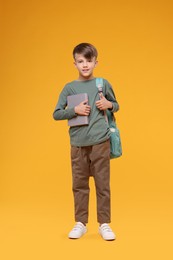 Photo of Cute schoolboy with book on orange background