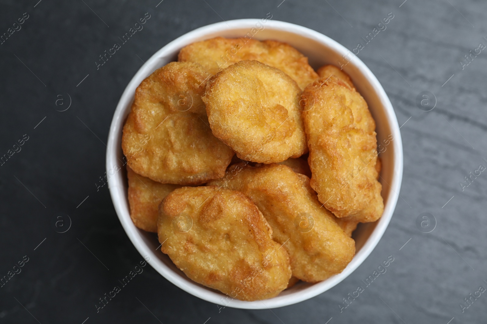 Photo of Bucket with tasty chicken nuggets on black table, top view