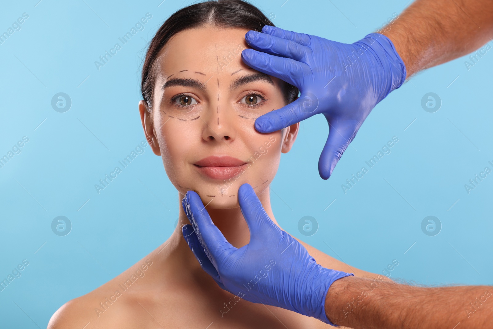 Photo of Doctor checking marks on woman's face for cosmetic surgery operation against light blue background