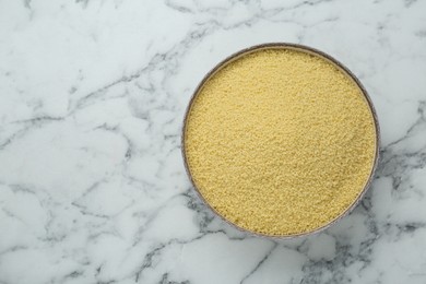 Photo of Bowl of raw couscous on white marble table, top view. Space for text