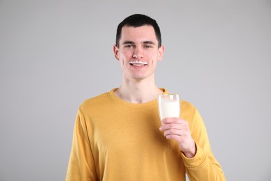 Happy man with milk mustache holding glass of tasty dairy drink on gray background