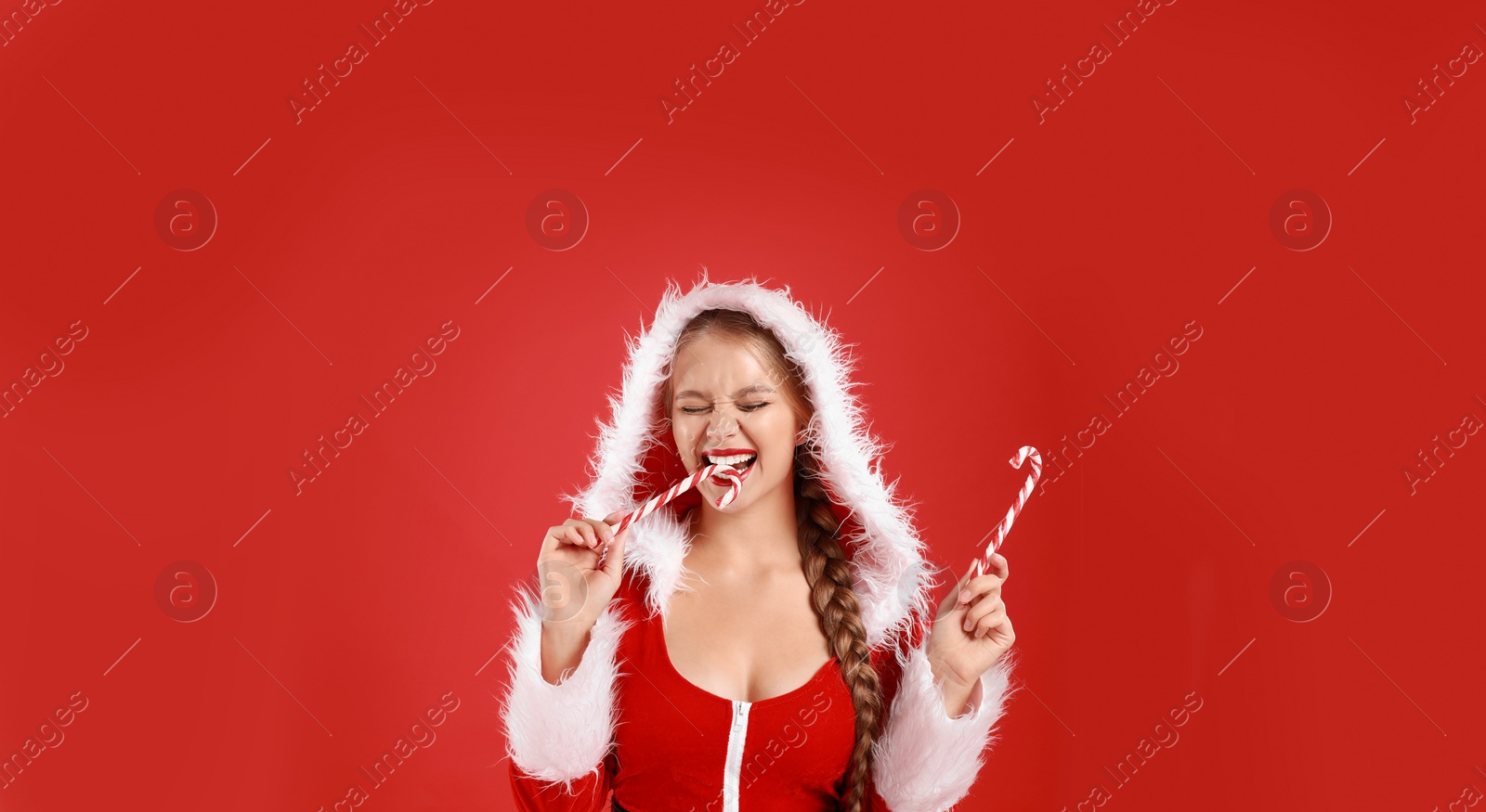 Photo of Beautiful Santa girl with candy canes on red background, space for text. Christmas eve