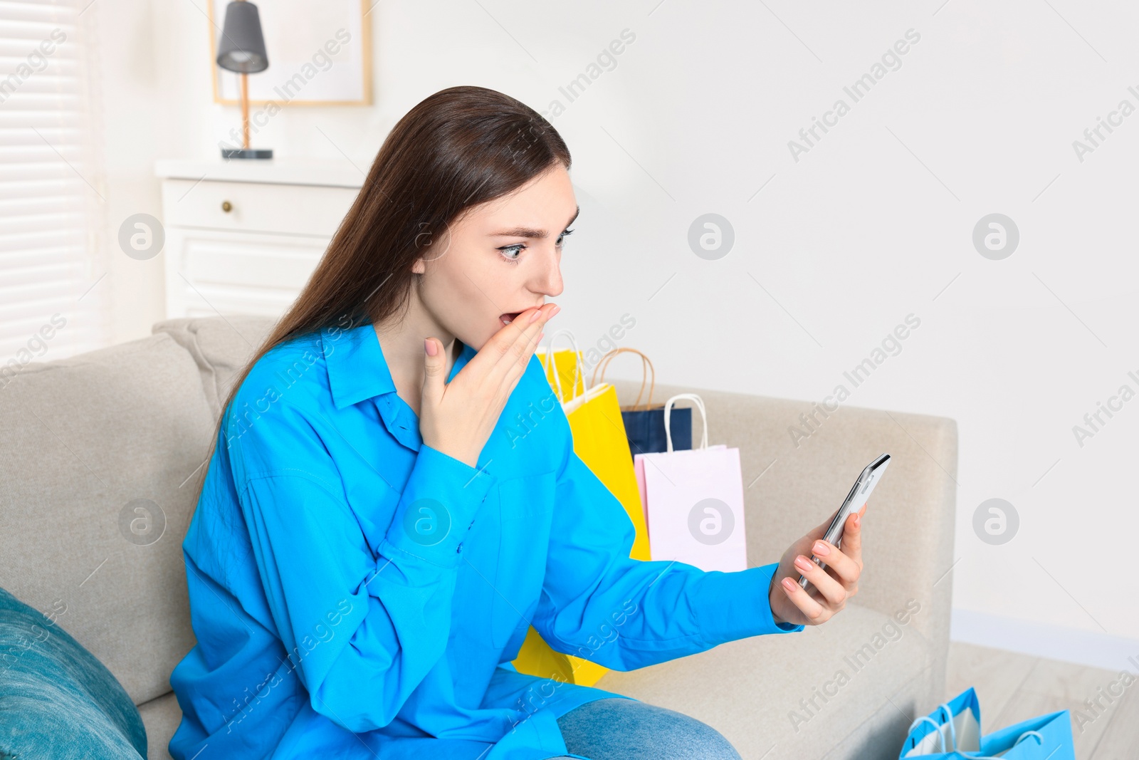 Photo of Special Promotion. Emotional young woman looking at smartphone on sofa indoors