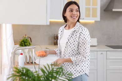 Photo of Happy young woman washing plate above sink in modern kitchen