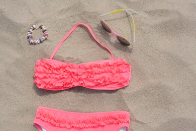 Photo of Sunglasses and bikini on sand, flat lay. Beach accessories