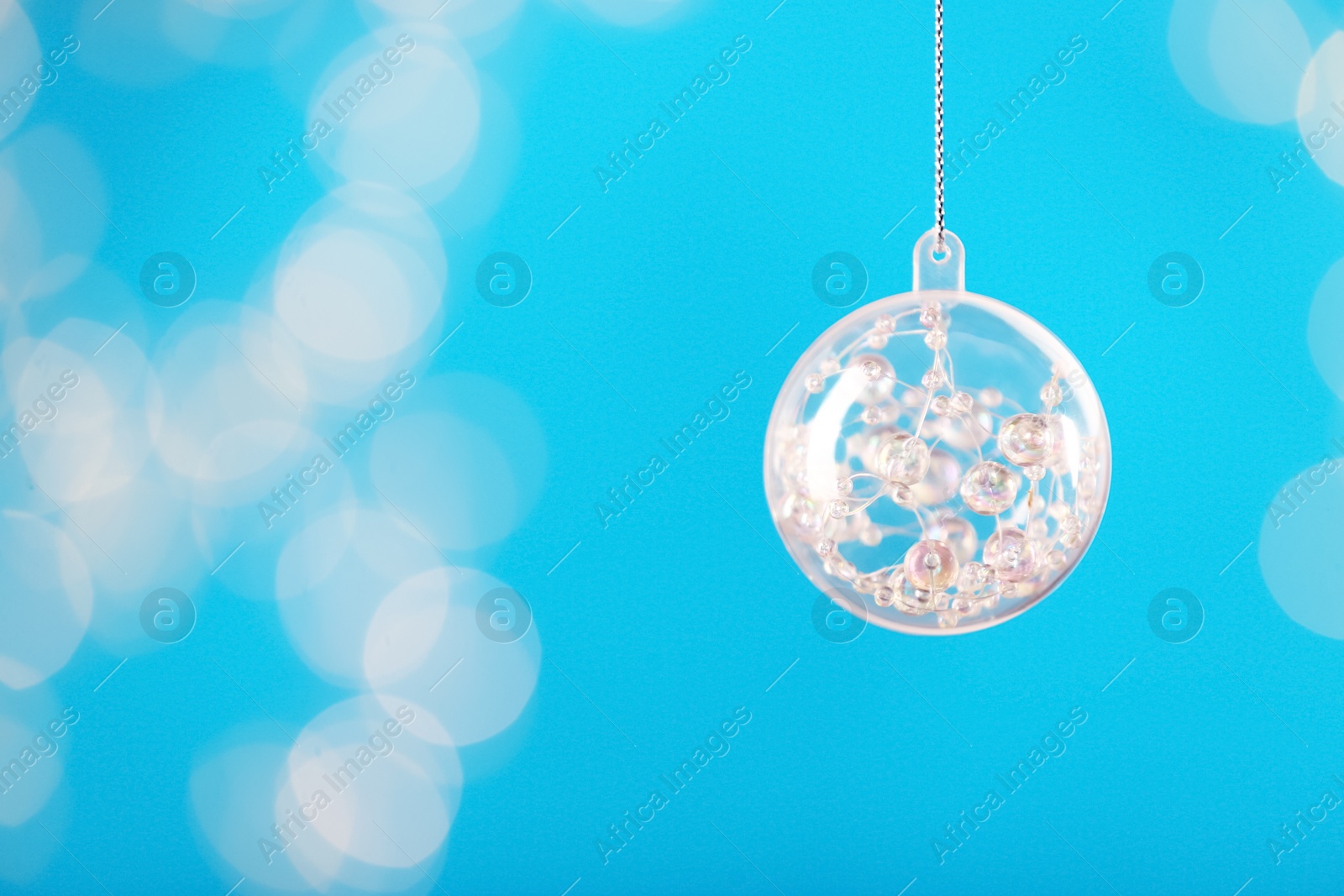 Photo of Decorative snow globe hanging on against blurred festive lights, space for text