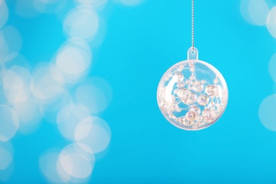 Decorative snow globe hanging on against blurred festive lights, space for text