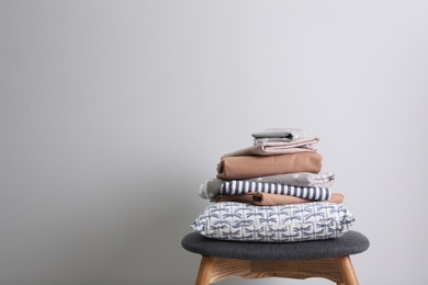 Photo of Stack of clean bed linen and pillow on stool near light grey wall. Space for text