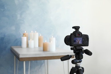 Photo of Professional camera and candles on table against color wall