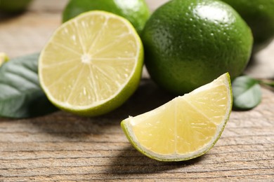 Whole and cut fresh limes on wooden table, closeup