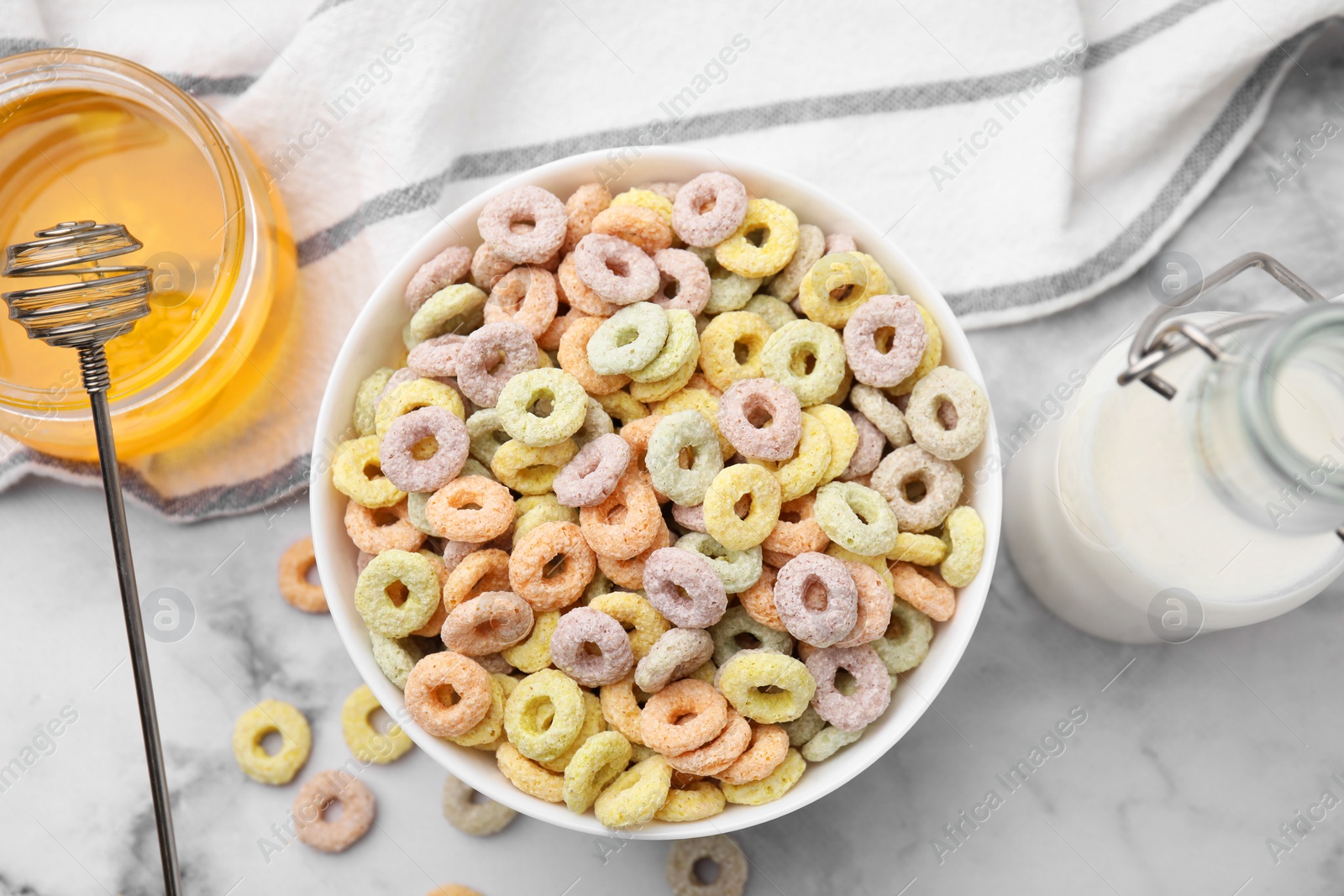 Photo of Tasty cereal rings in bowl, milk and honey on white marble table, flat lay