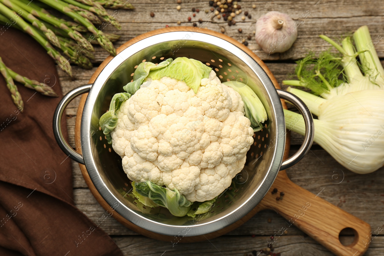 Photo of Metal colander with cauliflower, fennel and asparagus on wooden table, flat lay