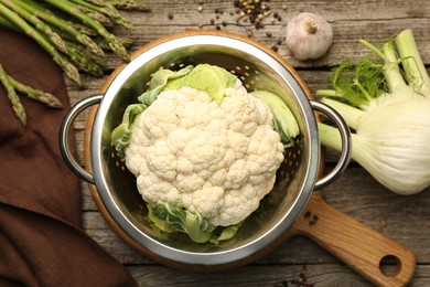 Photo of Metal colander with cauliflower, fennel and asparagus on wooden table, flat lay