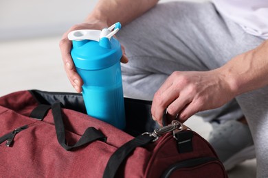 Photo of Young man putting shaker with protein into bag on blurred background, closeup