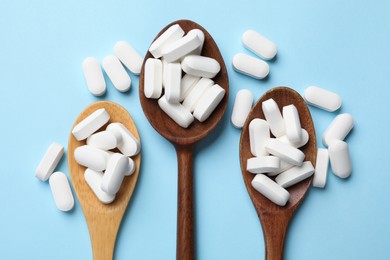 Photo of Vitamin capsules in wooden spoons on light blue background, flat lay