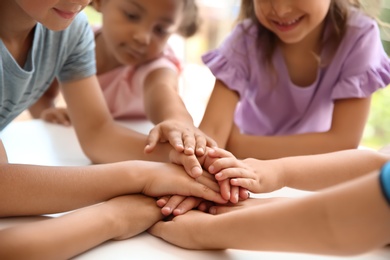 Photo of Little children putting their hands together at table, closeup. Unity concept