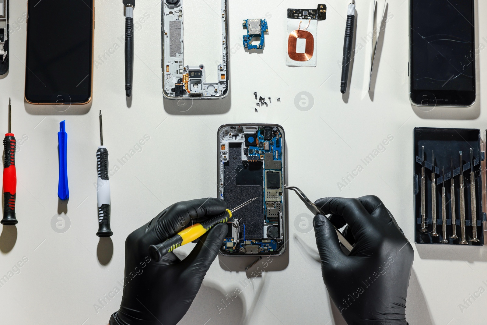 Photo of Technician repairing broken smartphone at white table, top view