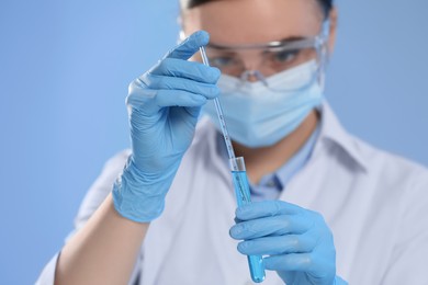 Scientist taking sample of light blue liquid on color background, closeup