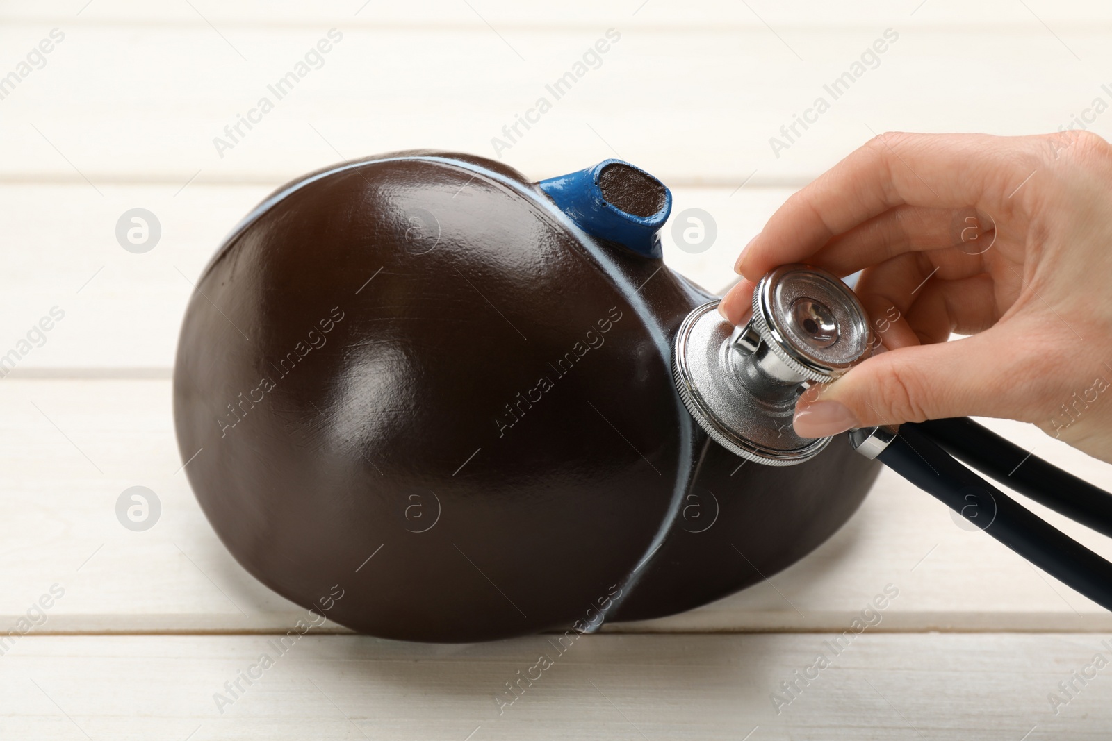 Photo of Doctor with stethoscope examining liver model at white wooden table, closeup