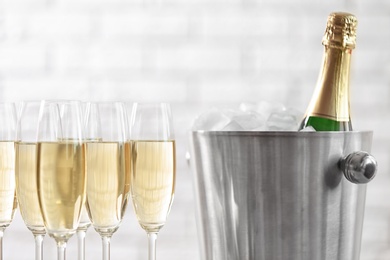 Glasses with champagne and bottle in bucket against blurred background. Celebration time