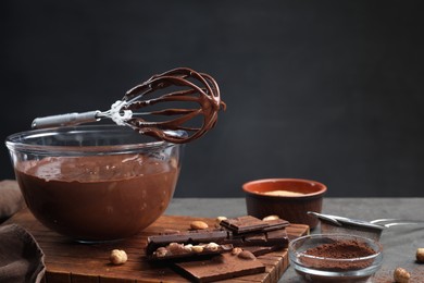 Photo of Bowl of chocolate cream, whisk and ingredients on gray table against dark background, space for text