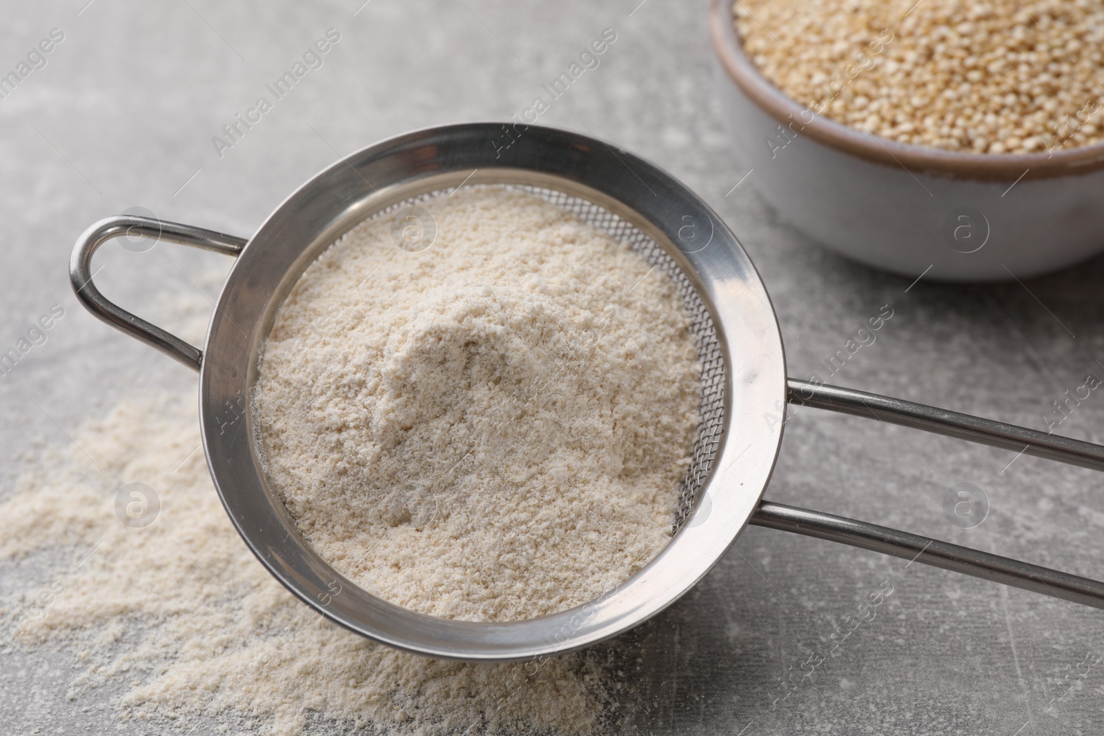 Photo of Sieve with quinoa flour on light grey table, closeup