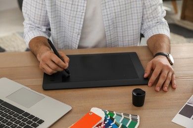 Photo of Professional designer with graphic tablet at wooden table, closeup