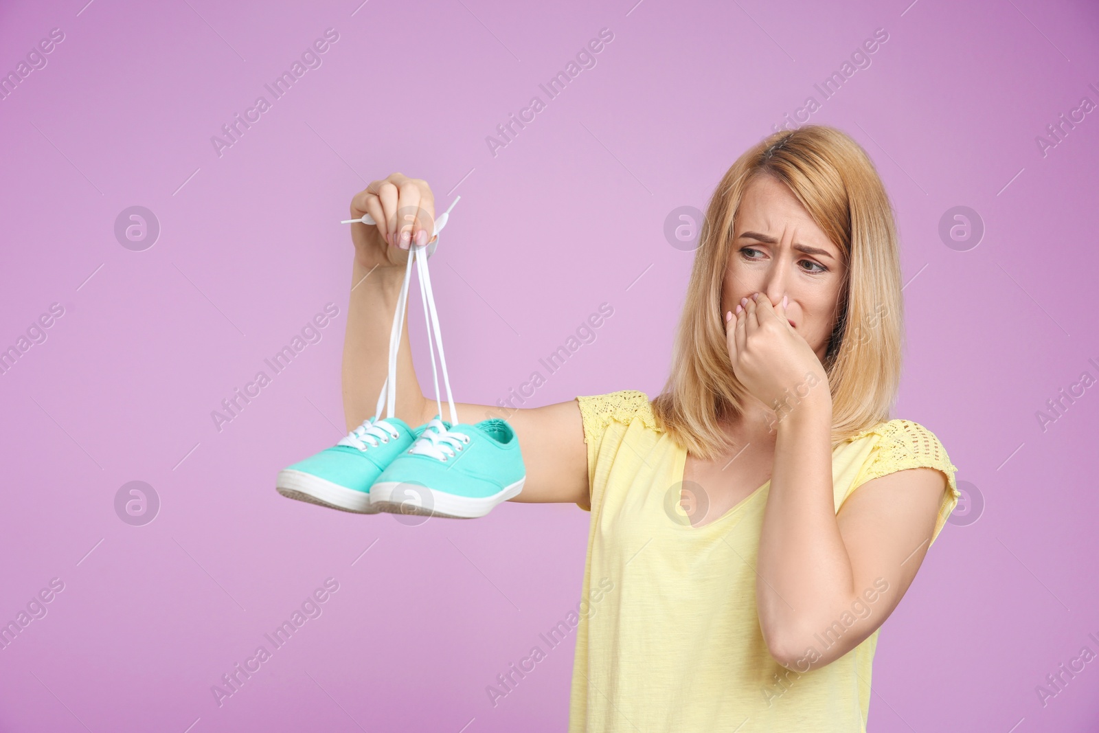 Photo of Young woman with stinky shoes on color background. Air freshener