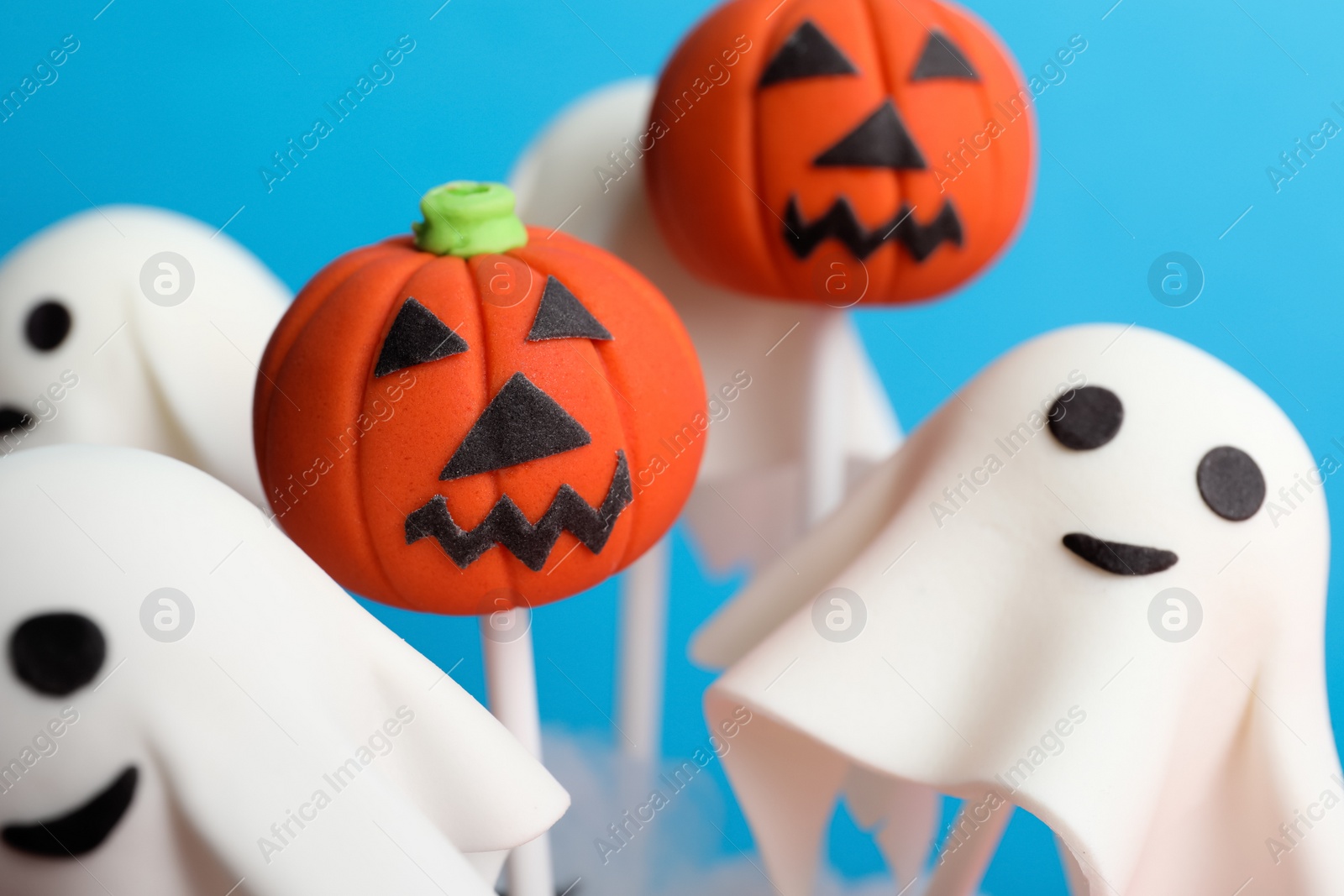 Photo of Delicious Halloween themed cake pops on light blue background, closeup