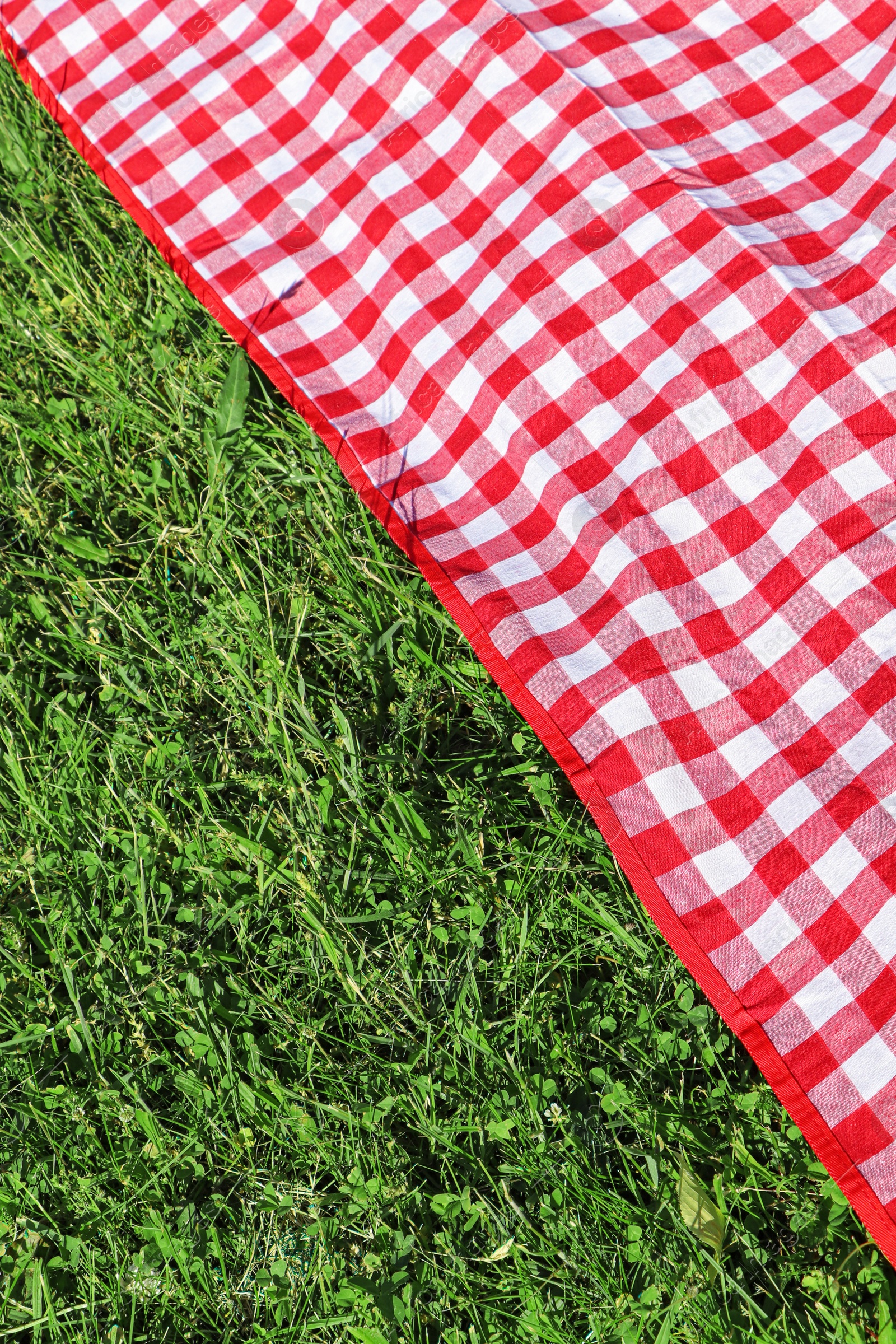 Photo of Checkered picnic tablecloth on fresh green grass, closeup. Space for text