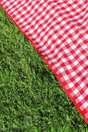 Checkered picnic tablecloth on fresh green grass, closeup. Space for text