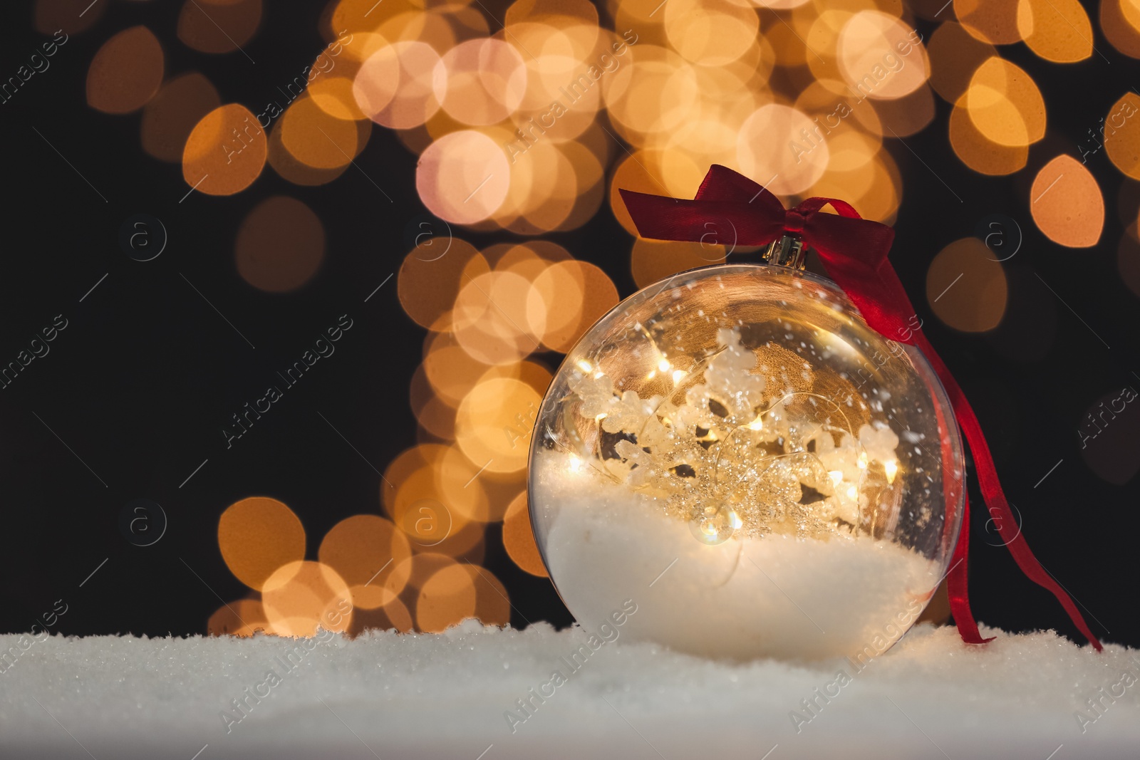 Photo of Decorative bright snow globe against blurred festive lights, closeup. Space for text