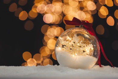Decorative bright snow globe against blurred festive lights, closeup. Space for text