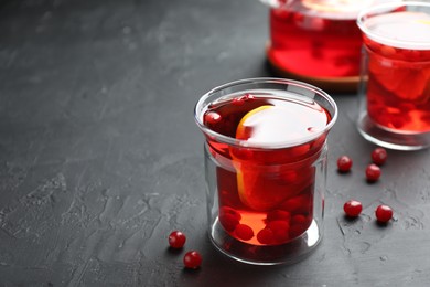 Photo of Tasty hot cranberry tea with lemon and fresh berries in glass on black textured table