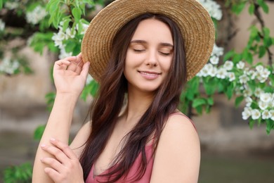 Photo of Beautiful woman in straw hat near blossoming tree on spring day