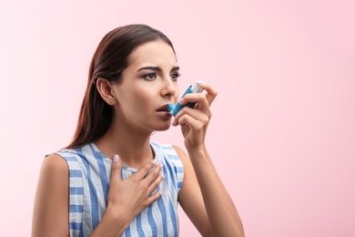 Young woman using asthma inhaler on color background. Space for text