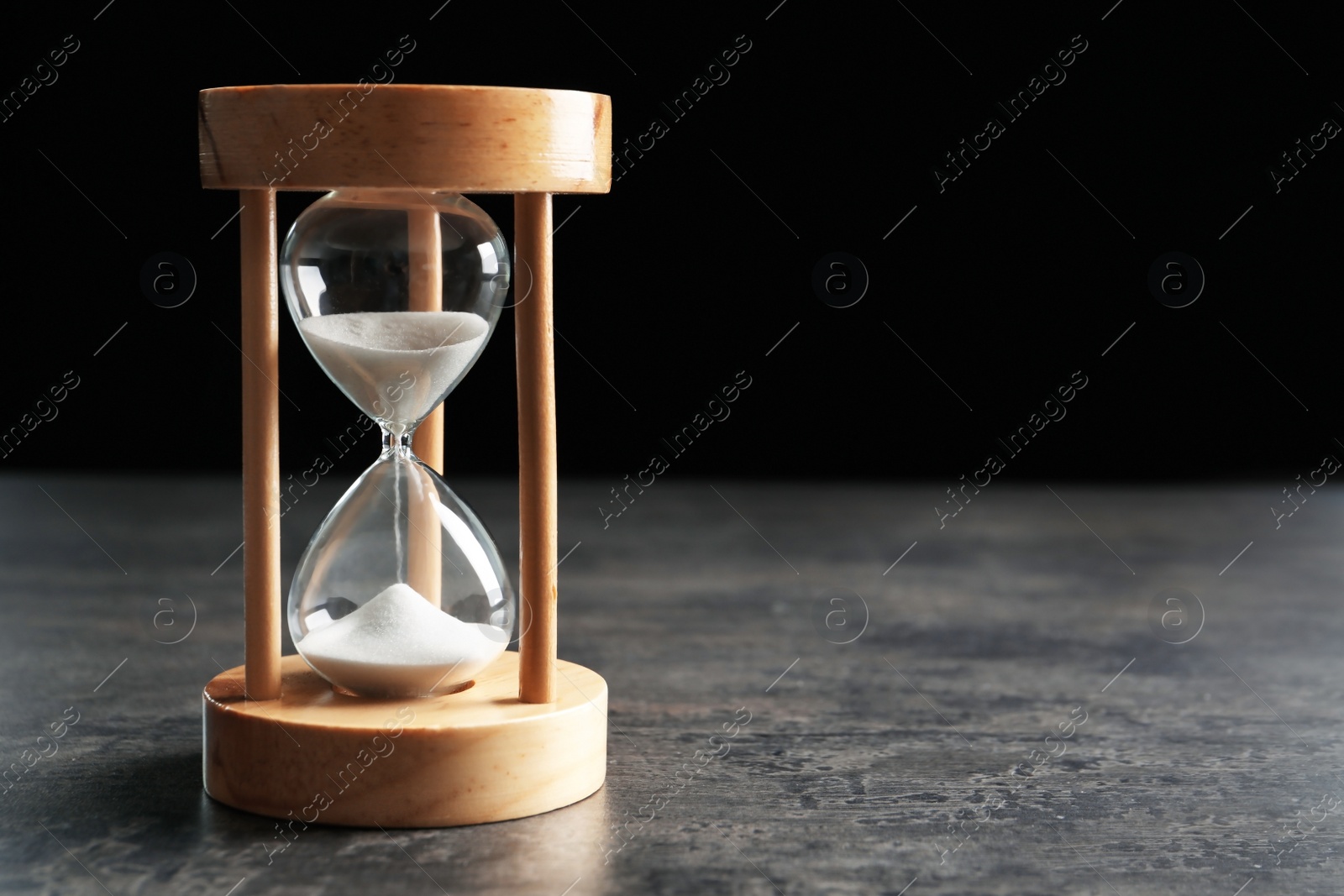 Photo of Hourglass with flowing sand on table against black background. Time management