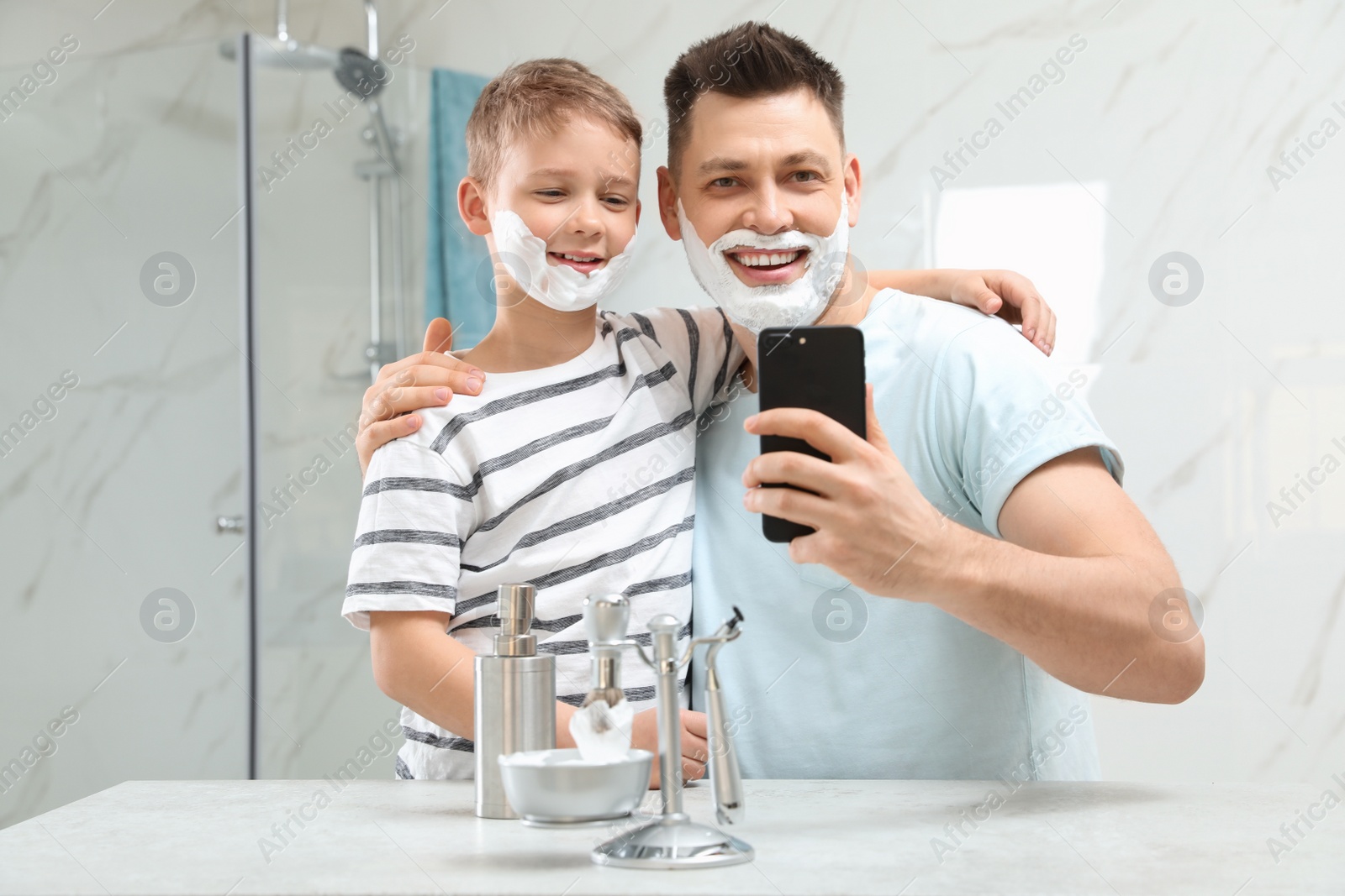 Photo of Son and dad with shaving foam on faces taking selfie in bathroom